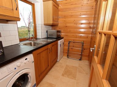 A utility room with washing machine microwave sink and wooden cabinets at Eagle Lodge Uig near Stornoway