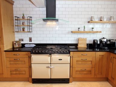 A kitchen with a stove oven range a black countertop wooden cabinets and white tiled wall at Eagle Lodge in Uig near Stornoway