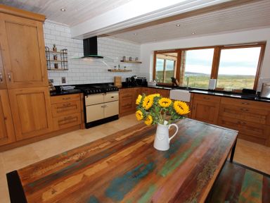 A kitchen with wooden cabinets a large window and a wooden table with sunflowers at Eagle Lodge in Uig near Stornoway
