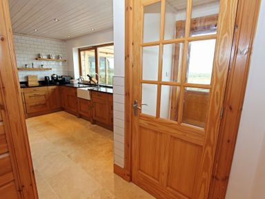 A kitchen with wooden cabinets a black countertop a window and a wooden door with glass panels at Eagle Lodge in Uig near Stornoway