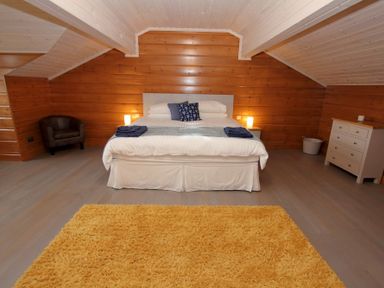 A bedroom with a bed and two bedside tables with lamps a yellow rug a chair and a dresser at Eagle Lodge Uig near Stornoway