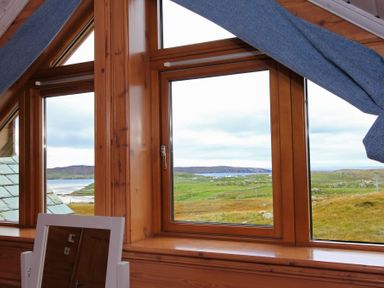 A wooden window with blue curtains overlooking a green landscape and water at Eagle Lodge in Uig near Stornoway