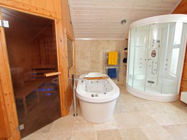 A bathroom with a freestanding bathtub a glass sauna and a shower cabin with towel racks at Eagle Lodge in Uig near Stornoway
