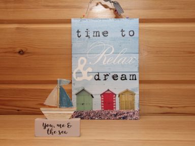 A wooden sign with the text time to relax and dream and a small wooden boat with the text you me and the sea on a wooden surface
