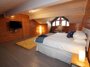 A bedroom with a bed a yellow rug a wall mounted tv and a dressing table at Eagle Lodge in Uig near Stornoway