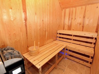A sauna room with wooden benches a wooden bucket and ladle and a heater with stones at Eagle Lodge in Uig near Stornoway