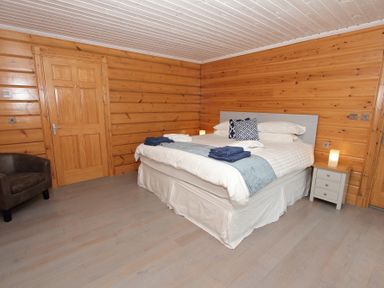 A bedroom with a double bed bedside tables lamps an armchair and wooden walls at Eagle Lodge in Uig near Stornoway