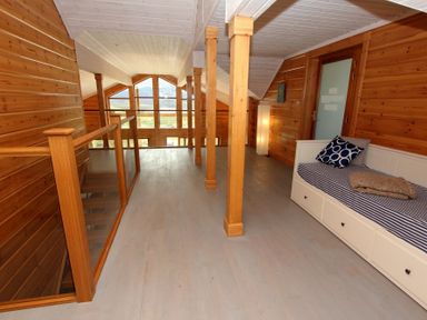 An upper floor hallway with wooden walls wooden pillars a white daybed and large windows at Eagle Lodge in Uig near Stornoway