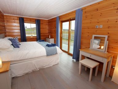 A bedroom with a bed blue curtains a dressing table and wooden walls at Eagle Lodge in Uig near Stornoway