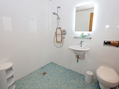 A bathroom with a shower, a wall-mounted sink, a toilet, a small trash bin, and tiled floor at Eagle Lodge in Uig near Stornoway