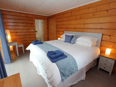 A bedroom with a large bed with white bedding and blue towels and pillows wooden wall panels and a small bedside table with a lamp at Eagle Lodge in Uig near Stornoway
