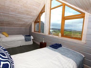 A bedroom with two single beds near large windows overlooking a green landscape at Eagle Lodge in Uig near Stornoway