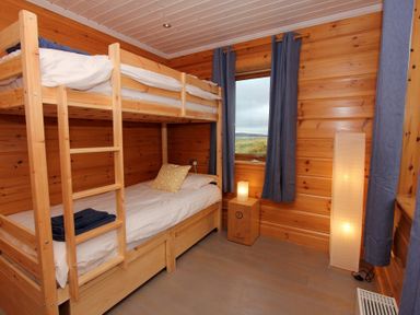 A wooden bedroom with bunk beds a pillow and folded towels a window with curtains and two lamps at Eagle Lodge in Uig near Stornoway