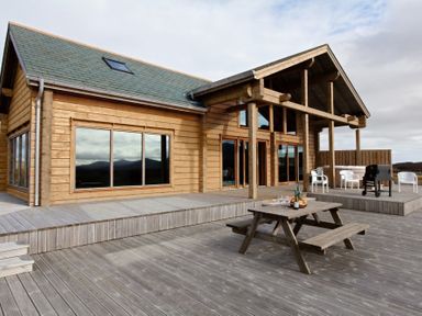 Exterior of a wooden house with large windows a deck with a picnic table chairs and a grill at Eagle Lodge in Uig near Stornoway