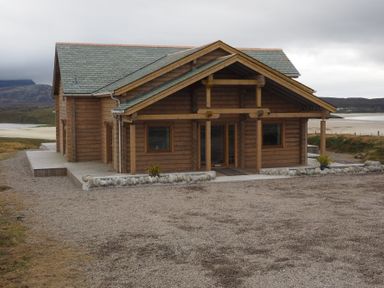 A wooden lodge with a peaked roof and gravel driveway near a beach at Eagle Lodge in Uig near Stornoway