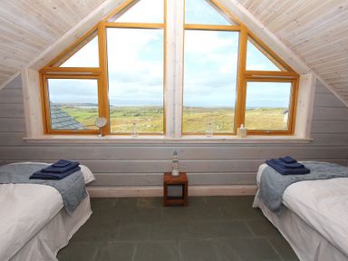 A bedroom with two single beds under slanted ceiling windows showing a landscape at Eagle Lodge in Uig near Stornoway