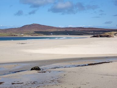 A sandy beach with small waves and hills in the background at Eagle Lodge in Uig near Stornoway