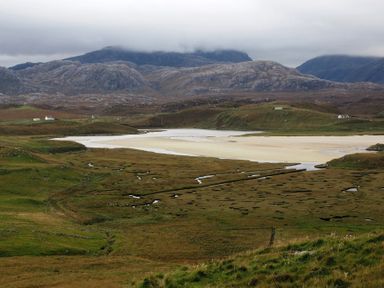 A landscape with grassy hills a wide sandy shore scattered houses and cloudy mountains in the background at Eagle Lodge in Uig near Stornoway