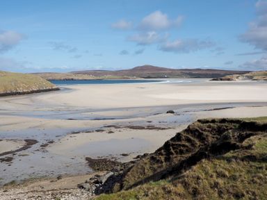A sandy beach with tidal pools and surrounding grassy hills at Eagle Lodge in Uig near Stornoway