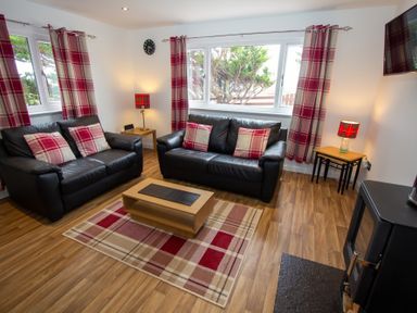 A living room with two black leather sofas red and white plaid cushions a wooden coffee table and plaid curtains at Braemore Chalet Tarbert Isle Of Harris