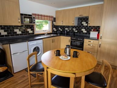 A kitchen with wooden cabinets black tiled backsplash round wooden table and chairs at Braemore Chalet Tarbert Isle Of Harris