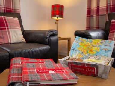 A living room with plaid pillows on leather sofas and a table with food basket and books at Braemore Chalet Tarbert Isle Of Harris