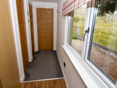 A hallway with wooden doors and a window showing an outdoor grassy area at Braemore Chalet in Tarbert Isle Of Harris