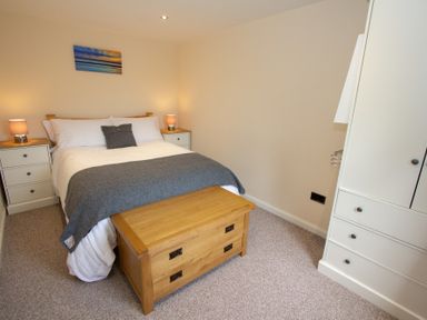 A bedroom with a double bed bedside tables wooden chest and white wardrobe at Braemore Chalet Tarbert Isle Of Harris