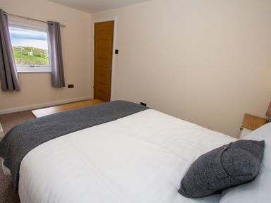A bedroom with a bed a window with curtains and a wooden door at Braemore Chalet Tarbert Isle Of Harris