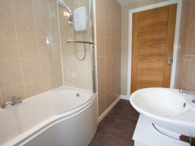 A bathroom with a bathtub shower combination and a white sink with a wooden door at Braemore Chalet Tarbert Isle Of Harris