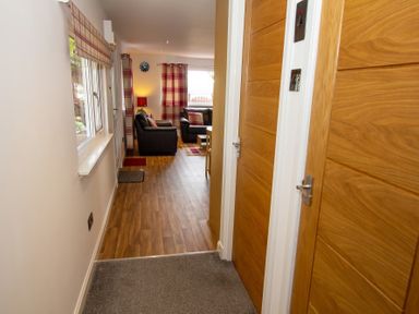 A hallway with wooden doors carpets and a window leading to a living room with sofas curtains and a clock at Braemore Chalet Tarbert Isle Of Harris