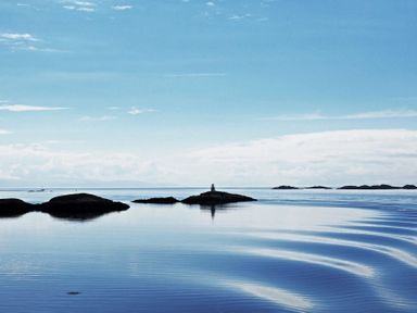 Calm sea with small rocky islands and a lighthouse under a blue sky at Braemore Chalet in Tarbert Isle Of Harris