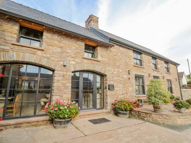 A stone exterior of a building with arched windows, doors, and flower pots at Pen Bont Home Farm in Upper Chapel near Builth Wells