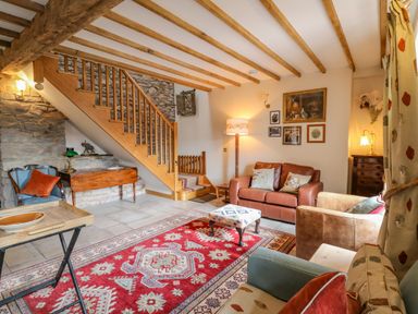 A living room with wooden stairs a red patterned rug and leather sofas at Pen Bont Home Farm Upper Chapel near Builth Wells