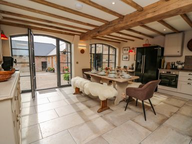 A kitchen with wooden beams a dining table with fur covered benches and chairs and large windows at Pen Bont Home Farm in Upper Chapel near Builth Wells