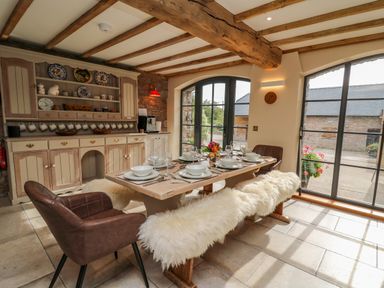 A dining room with a wooden table set for six people with chairs and benches covered in white fur at Pen Bont Home Farm Upper Chapel near Builth Wells