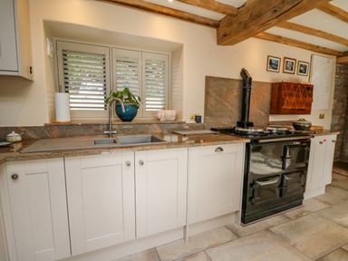 A kitchen with white cabinets a double sink a black stove and wooden ceiling beams at Pen Bont Home Farm in Upper Chapel near Builth Wells