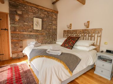 A bedroom with a bed with white linens and folded towels a stone wall with a framed picture and wooden beams at Pen Bont Home Farm in Upper Chapel near Builth Wells