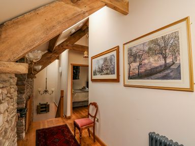A hallway with wooden beams, framed pictures on the wall, a chair, and a view into a bedroom at Pen Bont Home Farm Upper Chapel near Builth Wells