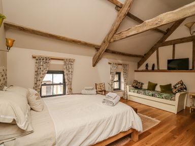 A bedroom with a bed and sofa under a sloped ceiling with exposed wooden beams at Pen Bont Home Farm in Upper Chapel near Builth Wells
