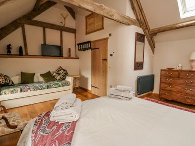 A bedroom with exposed wooden beams a bed with towels a couch with patterned cushions a wooden dresser and a mirror at Pen Bont Home Farm Upper Chapel near Builth Wells