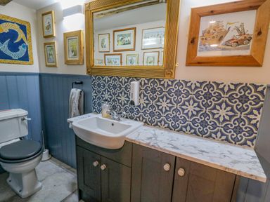 A bathroom with a toilet a sink with cabinet and a mirror above the sink with blue patterned tiles and framed pictures on the wall at Pen Bont Home Farm Upper Chapel near Builth Wells