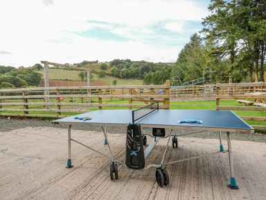 An outdoor ping pong table on a concrete surface with playground swings and slides in the background at Pen Bont Home Farm in Upper Chapel near Builth Wells