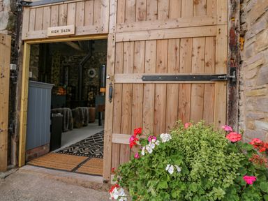 A wooden barn door open showing interior with furniture and plants outside at Pen Bont Home Farm in Upper Chapel near Builth Wells