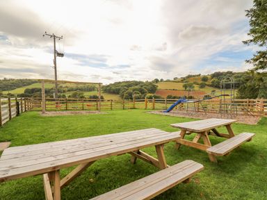 An outdoor playground with swings slide climbing frame and wooden picnic tables at Pen Bont Home Farm in Upper Chapel near Builth Wells