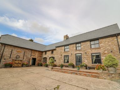 A stone building with multiple windows and doors with flower pots in front at Pen Bont Home Farm Upper Chapel near Builth Wells