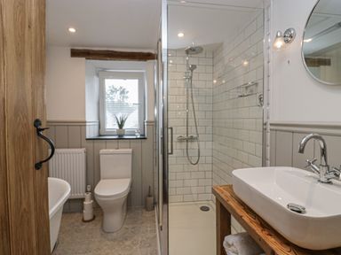 A bathroom with a toilet near a window a glass shower enclosure and a sink on a wooden countertop at Style Cottage in Keswick