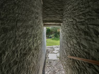A stone corridor with a wooden handrail leading to a garden at Style Cottage in Keswick