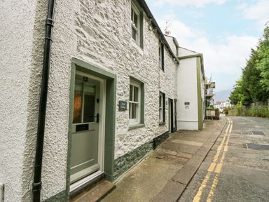 A stone exterior cottage with a green door and windows along a narrow street at Style Cottage in Keswick