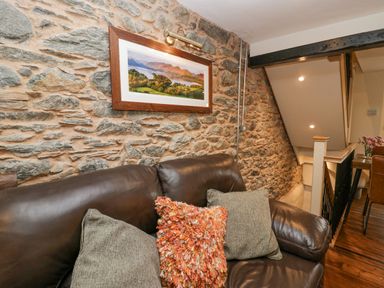 A brown leather sofa with cushions against a stone wall with a framed landscape picture above at Style Cottage in Keswick